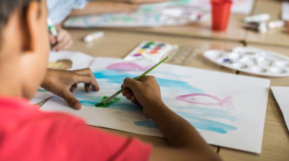 Close up of elementary student using watercolors for painting on art class in the classroom.
