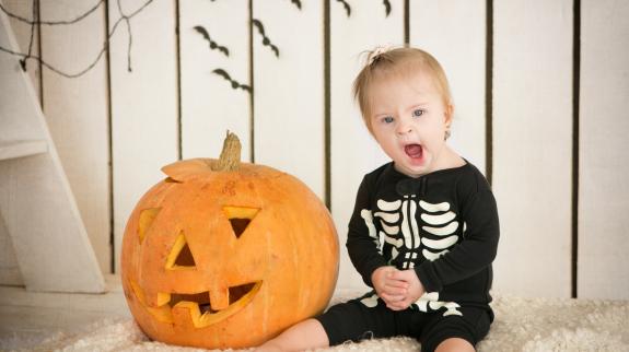 Little girl sitting dressed as a skeleton sitting near a jack-o-lantern pumpkin.