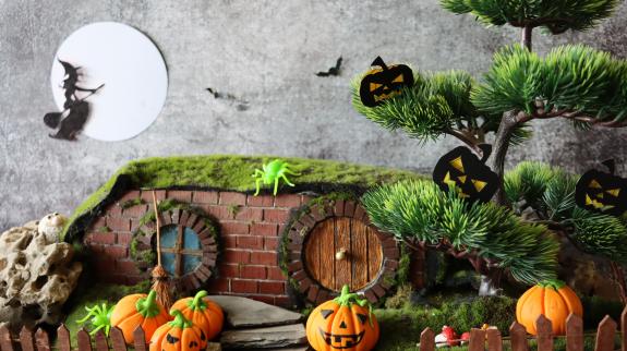 A Halloween diorama night scene with witch flying on broom across full moon, jack-o-lanterns, and bats.