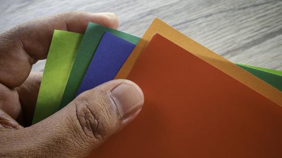 Hand holding a fan of colorful origami paper sheets, a vibrant craft project.