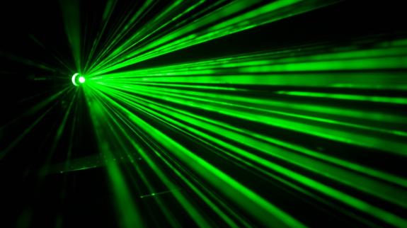 Striking green laser beams radiate from a single point of origin, a laser gun, on the left. 