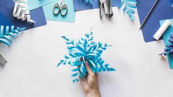 Top down view of hands making three dimensional paper snowflake decorations.