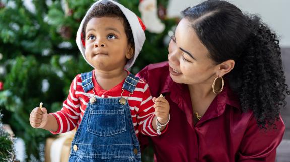 Mother and toddler son play together near Christmas tree.
