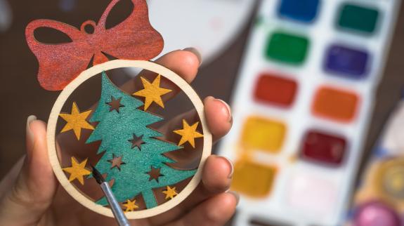 Person paints a wooden ornament to hang on a tree.