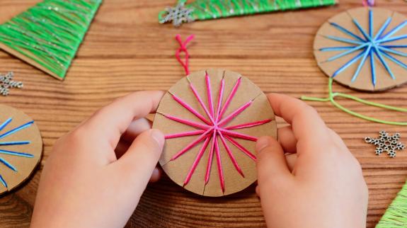 Child's hands making yarn wrapped cardboard Christmas ornaments.