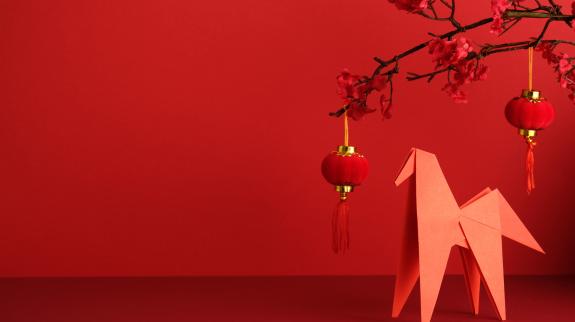 An origami paper horse, red lantern, and plum blossom branch against a bright red background. 