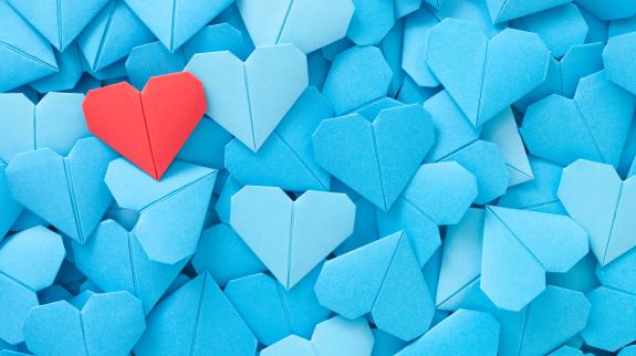 Blue origami hearts with one single red heart on top of pile.
