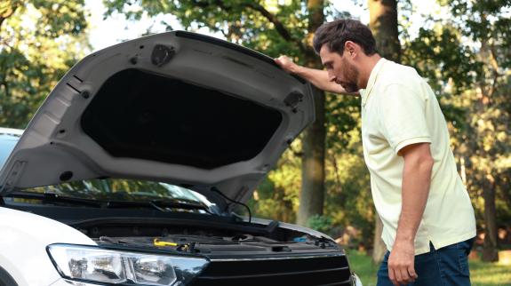 Man looking under hood of car outdoors.