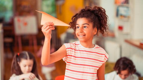 A smiling girl launching her paper plane.