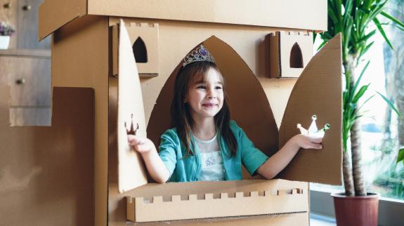 Child dressed as princess playing in a cardboard fort.
