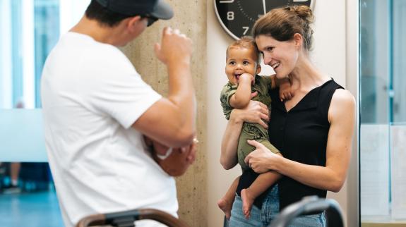 Mingling after Storytime at Terry Fox Library: a man waves to a a baby being held in his mother's arms.