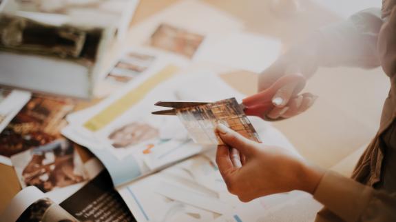 Pair of hands with scissors cuts out magazine pictures to make collage.