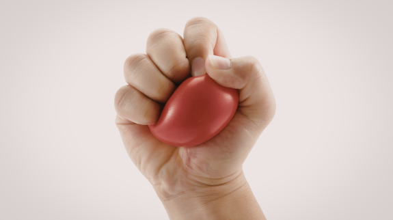 Pale hand squishing a red stress ball on a beige background.