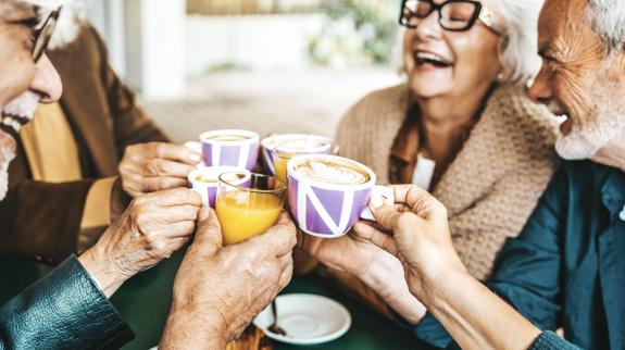 Senior people group toasting with lattes at coffee bar.