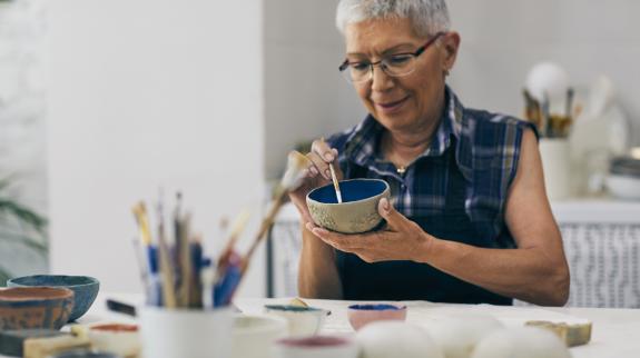 Senior woman decorating bowl made of clay on ceramics workshop.