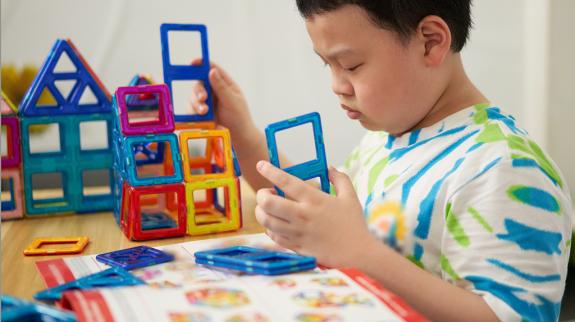 Young boy builds using magnetic Magformer pieces.