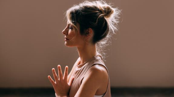 A side view of a female athlete in sports clothes meditating.