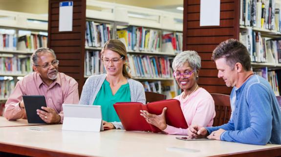 Group of adults in library looking at tablets at a table