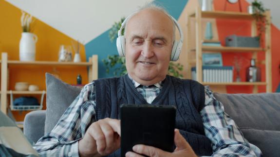 A older man sitting in a living room in headphones using a smart phone
