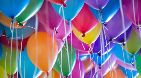 Festive, colorful balloons with filled with helium and attached to the white ribbons.