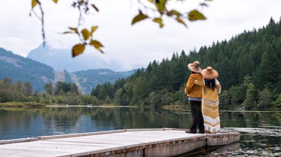 An indigenous man and woman standing on a dock looking out onto the lake.