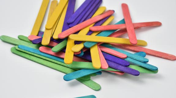 Multi-coloured wooden popsicle sticks sit in a big pile on table.