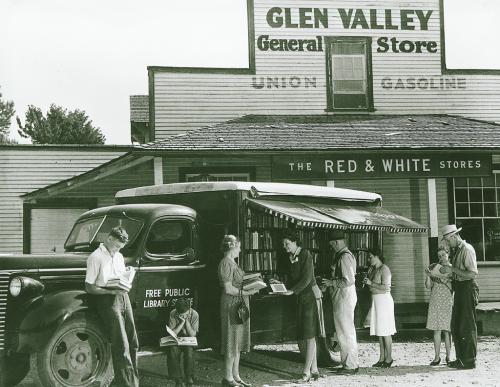A crowd of people outside a store, socializing and acquiring books from library on wheels book van.