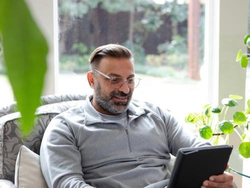 A man sitting comfortably in a chair, relaxed and engaged with his tablet.