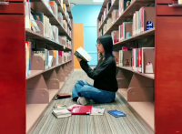 Image of person sitting down looking at books between book shelves.