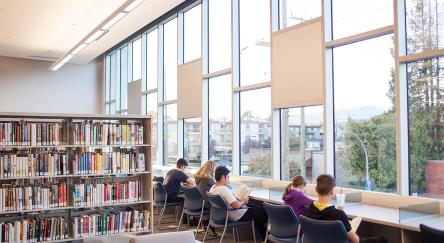 Readers in the library's desk facing a wide window.