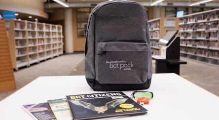 A backpack placed on a table in a library, with shelves of books visible in the background.
