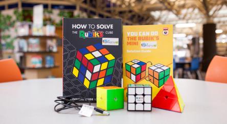 Various Rubik's cubes on a table next to books about Rubik's cubes.
