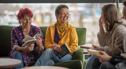 Three women sit comfortably on a couch, discussing the book they are reading and sharing a moment of literary enjoyment.