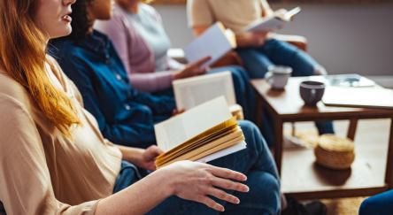 Diverse group of people sitting in a circle, holding open books, actively talking and exchanging thoughts, creating a sense of community and engagement.