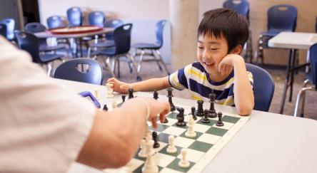 A young boy and an adult engaged in a friendly game of chess, focused on their strategy and moves.