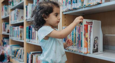 A young girl selects a picture book off the shelf at Abbotsford Community Library.