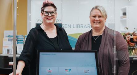 Two women, working as librarians at Fraser Valley Regional Library, stand in front of a computer screen, focused on their task.