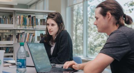 Two students in a library work on laptops, exploring LinkedIn Learning to enhance their knowledge and skills.