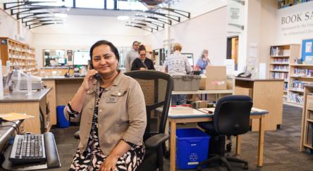 A woman at her desk, talking on the phone, appearing attentive and engaged in the conversation.