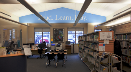 Interior of Dean Drysdale Library with feature wall that reads "Read Learn Play" above rows of bookshelves.