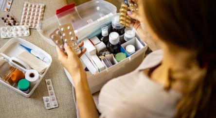 A woman on a couch examines a box of medicine, highlighting the importance of consumer health.