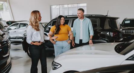 A dad and daughter explore a car showroom, discussing options and reviewing consumer reports for their next vehicle purchase