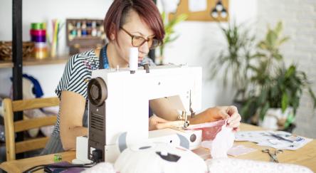 A woman is engaged in sewing a stuffed animal, highlighting her artistic flair and dedication to handmade crafts.