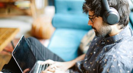 A man with headphones sits on a couch, engaged in learning with Mango Languages.