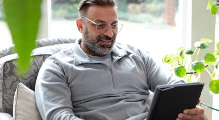 A man sitting comfortably in a chair, relaxed and engaged with his tablet.