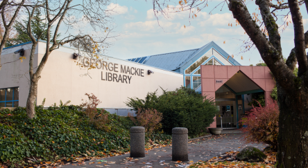A leafy tree stands in front of the George Mackie Langley Library in North Delta, showcasing its vibrant exterior.