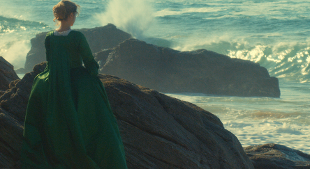 A woman wearing a green dress poses on a rock, showcasing her elegance against a natural backdrop.