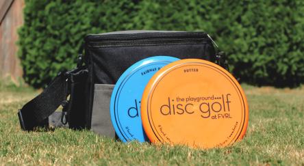 Golf discs alongside a bag of golf discs placed on lush green grass, perfect for outdoor fun.