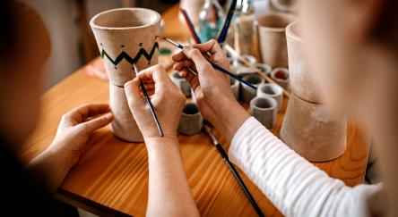 Two individuals collaborate on painting small flower pots sharing in a cozy workspace.