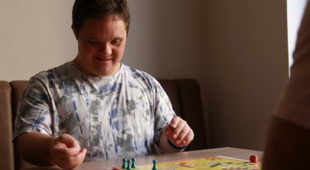 A man and his friend enjoy a lively board game, sharing laughs over the game board.